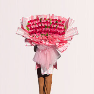 A large, opulent bouquet of pink and red roses is held by a person against a light, off-white background.
